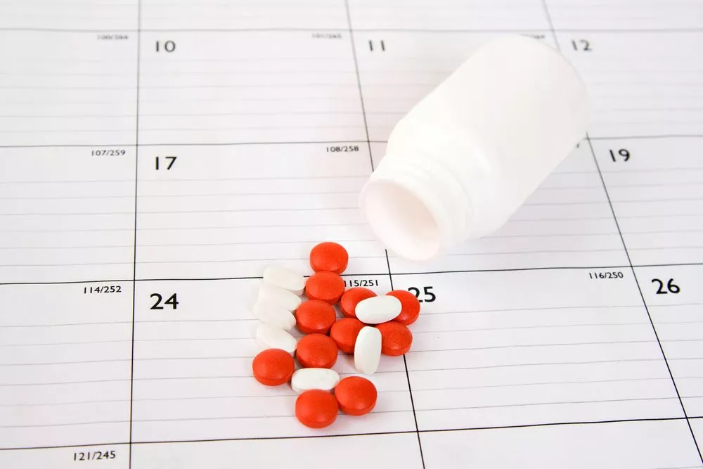 pills spilling out of bottle on top of a calendar