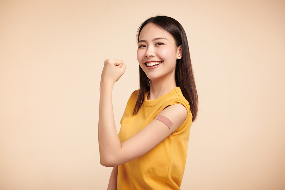 young woman smiling and showing off arm with bandage after vaccine shot