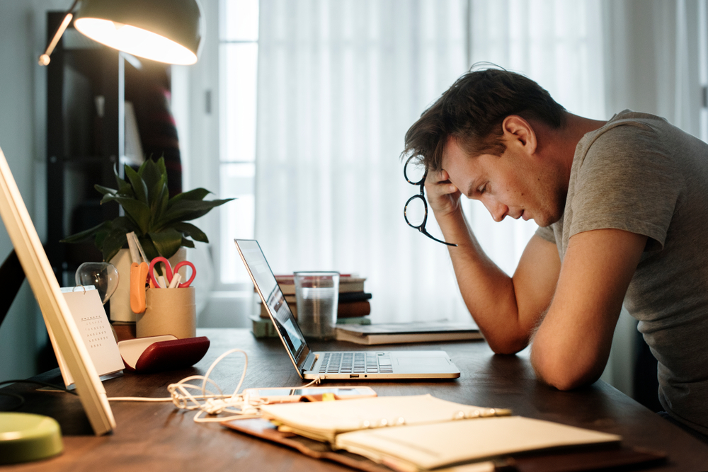 stressed man holding head while looking at laptop at work desk